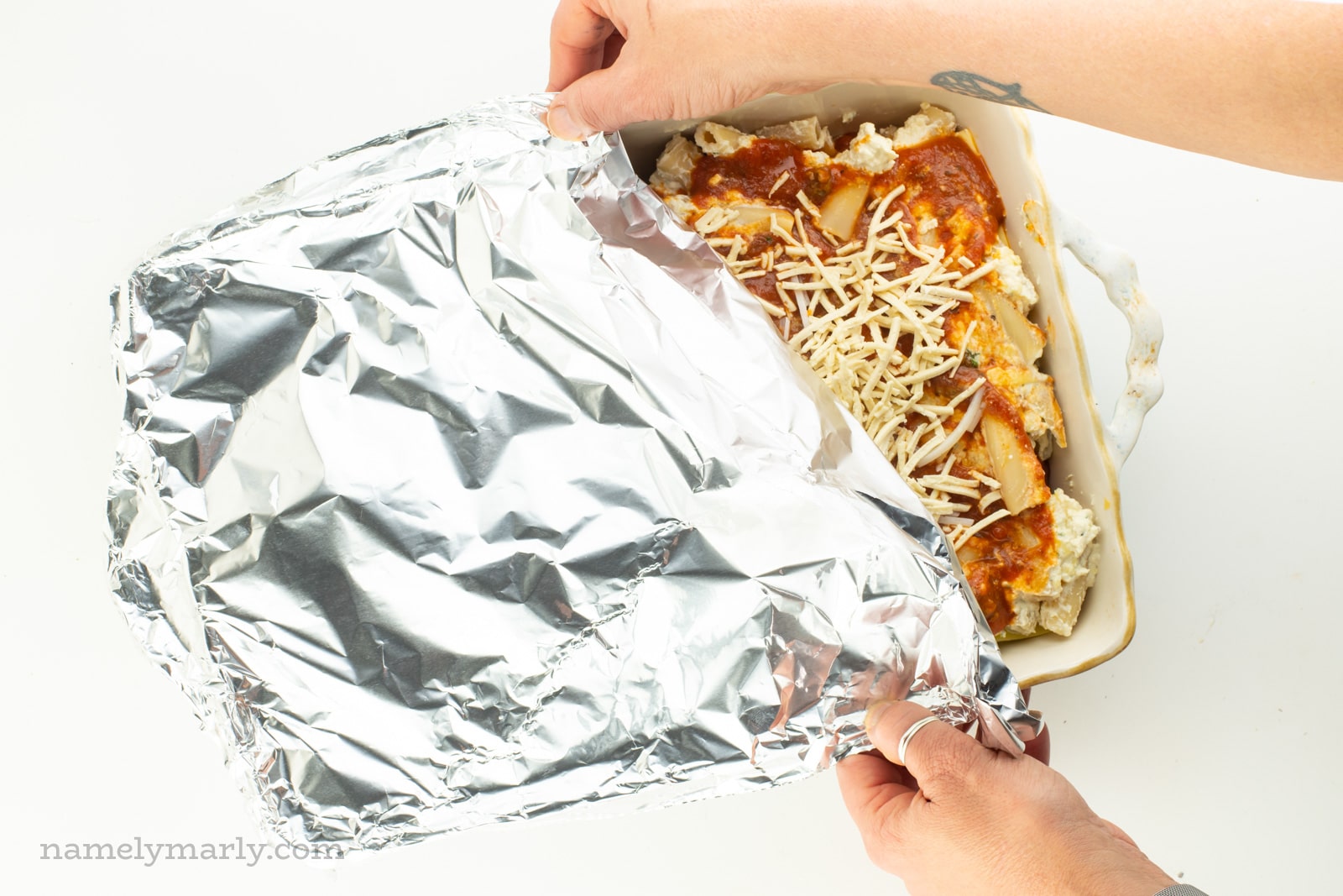 Two hands reach in and cover an unbaked dish of meatless ziti with foil.