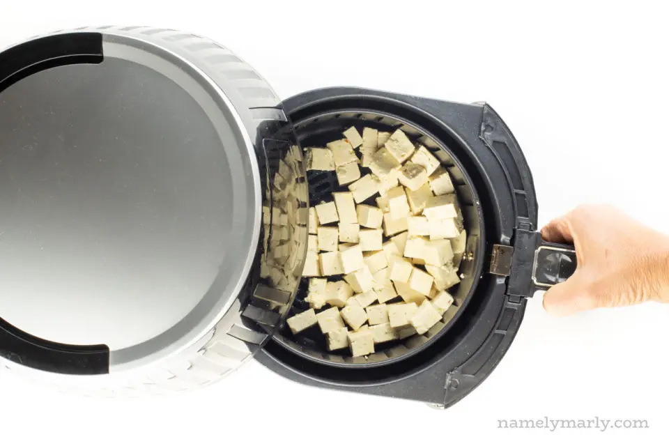 Tofu cubes are in an air fryer basket.