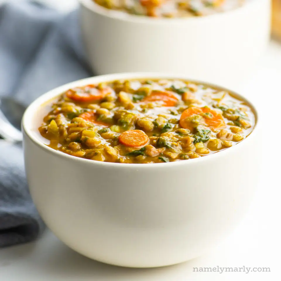 A bowl of curried lentil soup shows chopped carrots and spinach in the bowl.