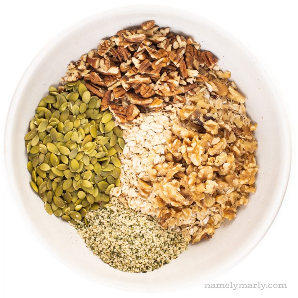 A large white bowl holds oats, nuts, and seeds used for making protein granola.