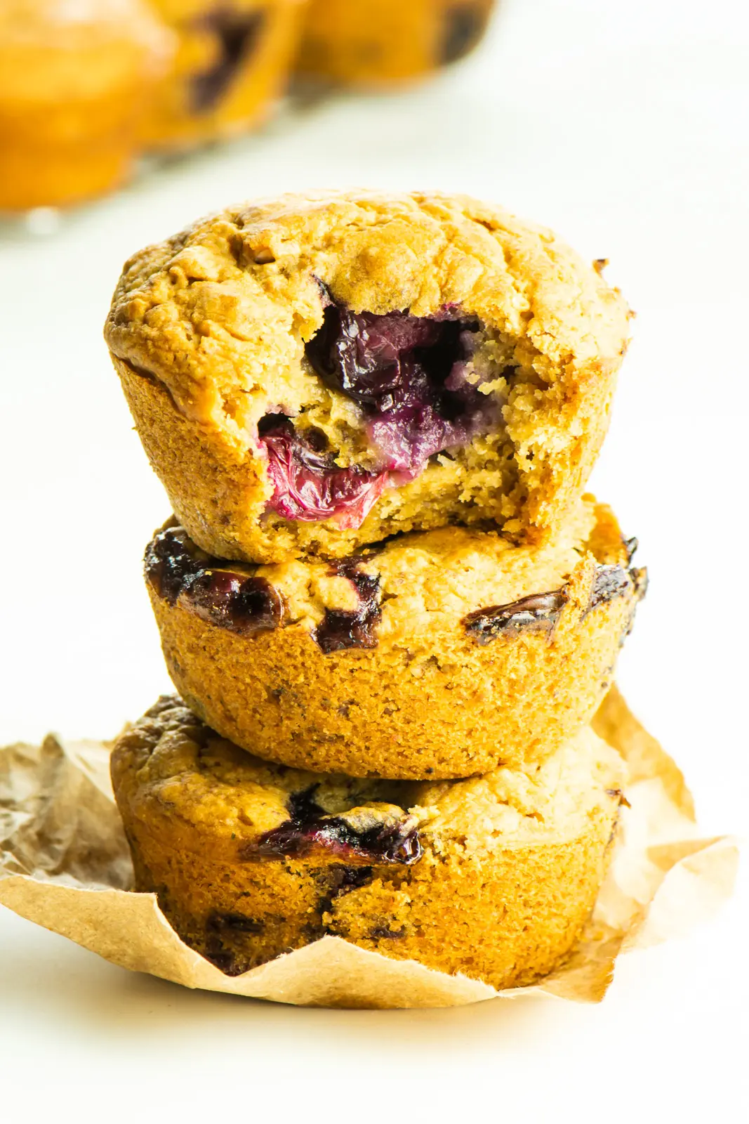 Three vegan blueberry muffins are stacked on top of each other and a bite is taken out of the top one.