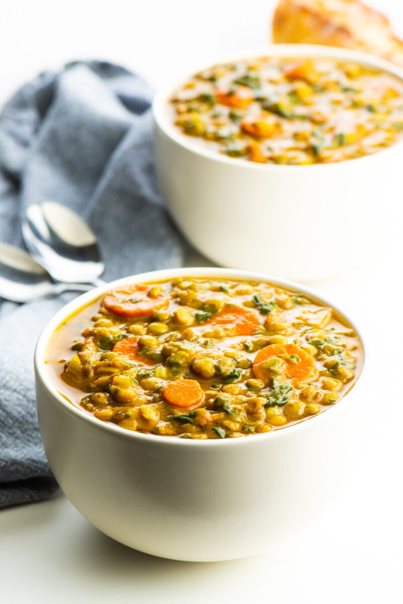Two bowls of curried lentil soup with a loaf of crusty bread behind it.