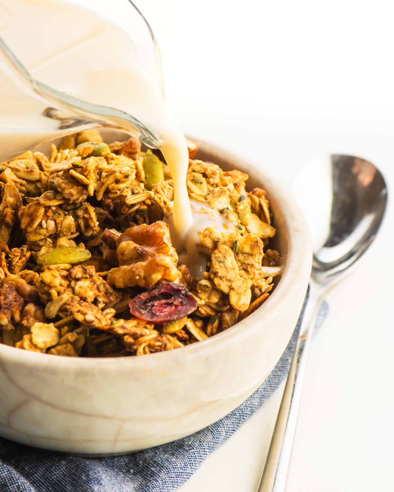 A bowl full of protein cereal with almond milk being poured int it.