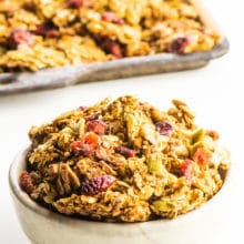 A bowl of protein granola sits in front of a pan with the rest of the granola, fresh from the oven.