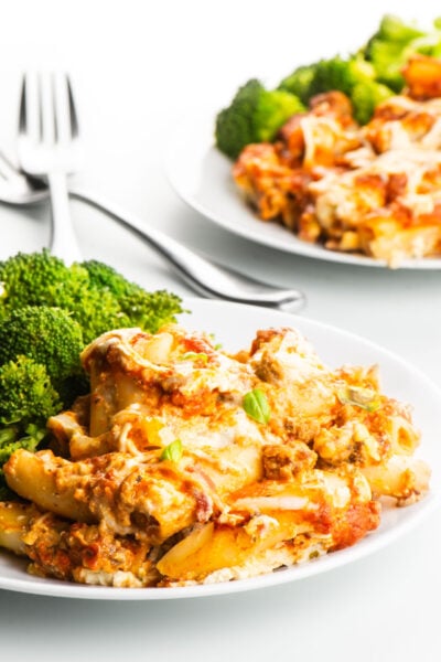 Two plates of meatless baked ziti and steamed broccoli with forks between them.