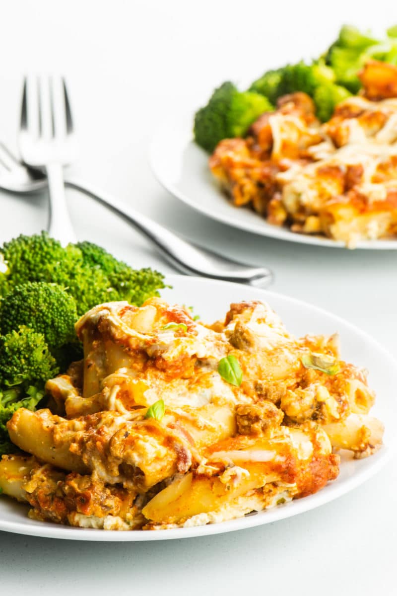 Two plates of meatless baked ziti and steamed broccoli with forks between them.