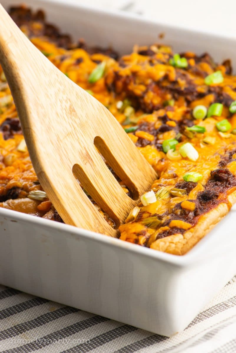 A spatula digs into a casserole dish with vegan baked hot dogs.