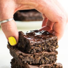A hand reaches in and grabs the top brownie in a stack of three.