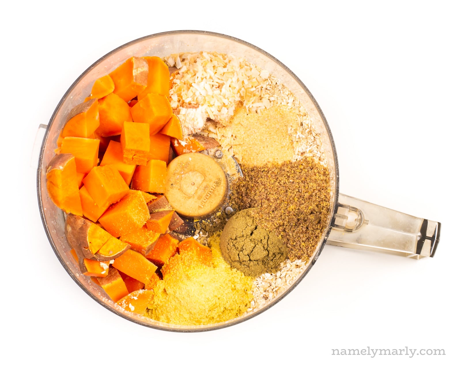 Ingredients like sweet potatoes and ground flax seeds are in a food processor bowl.