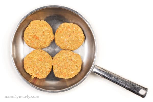 Four vegan chicken patties are in a stainless steel frying pan.