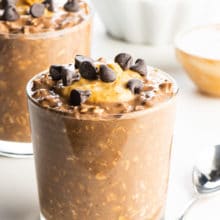 A glass full of chocolate peanut butter overnight oats topped with peanut butter and chocolate chips.