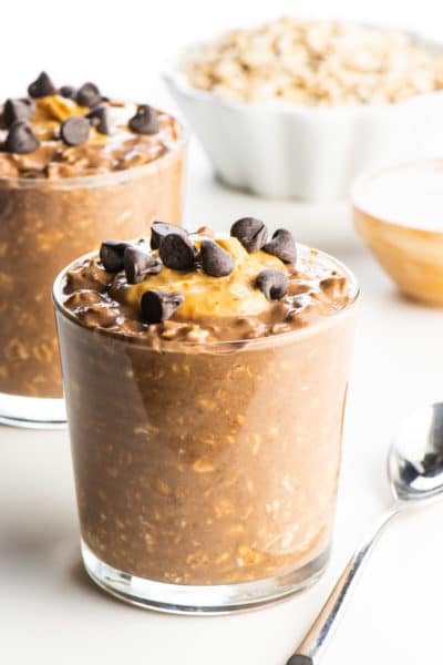 A glass full of chocolate peanut butter overnight oats topped with peanut butter and chocolate chips.