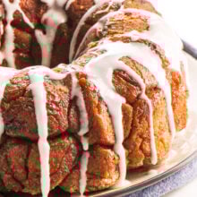A loaf of Vegan Monkey Bread sits on a plate with lots of frosting drizzled over the top.