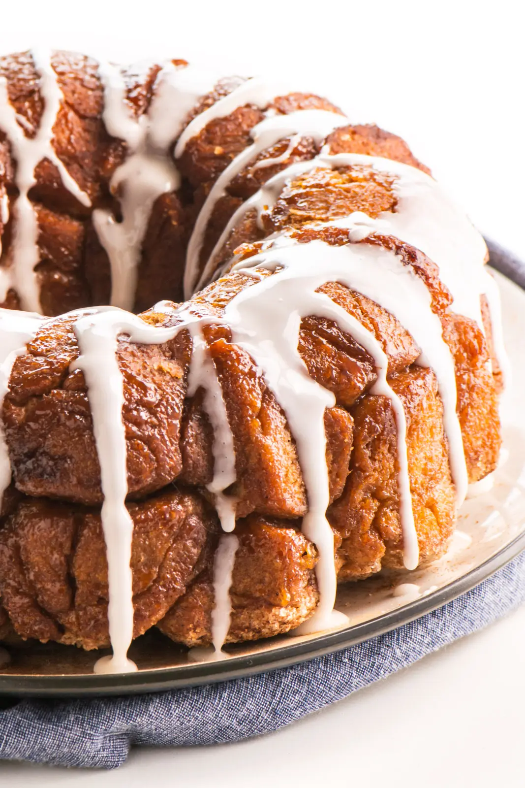 A loaf of Vegan Monkey Bread sits on a plate with lots of frosting drizzled over the top.