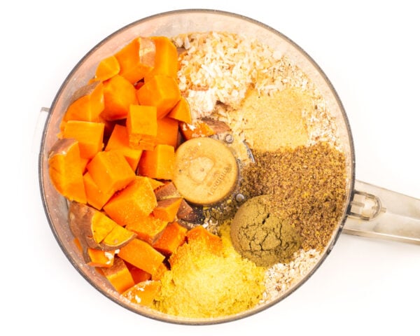 Ingredients like sweet potatoes and ground flax seeds are in a food processor bowl.