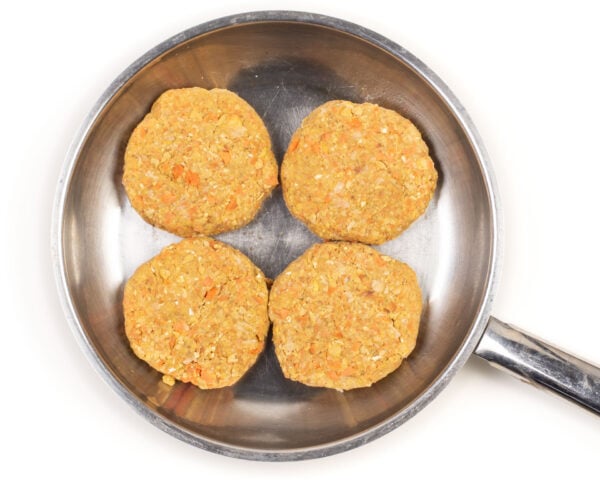 Four vegan chicken patties are in a stainless steel frying pan.