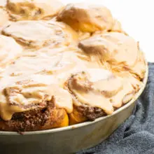 A batch of freshly baked and frosted cinnamon rolls in a pan sit on a dark blue kitchen towel.