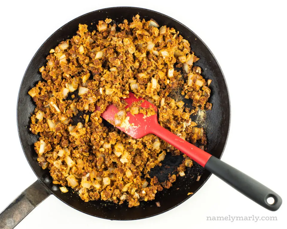 Veggie crumbles in a skillet with a red spatula.