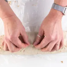 Two hands are pinching a log of dough to create a seam.