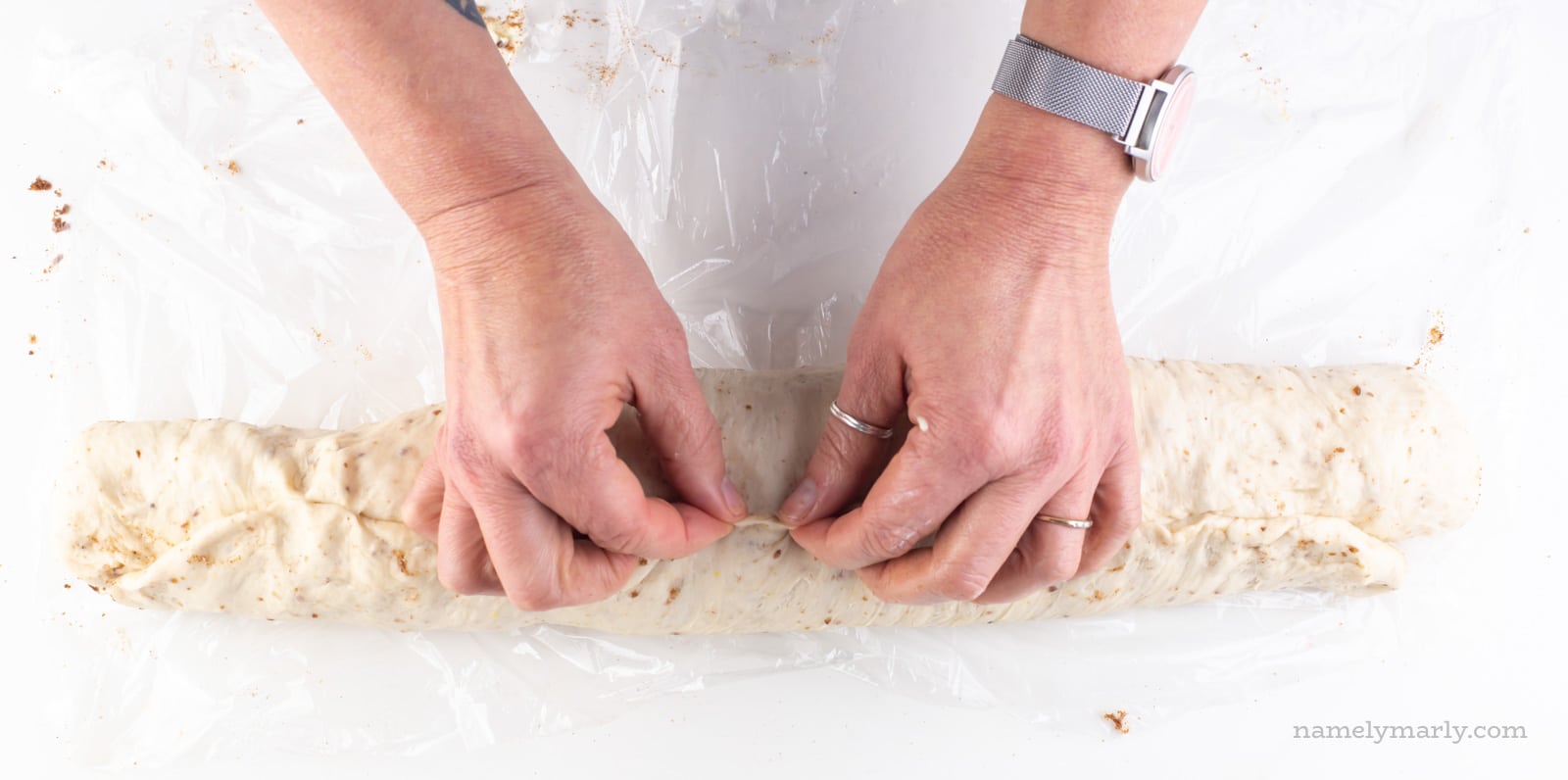 Two hands are pinching a log of dough to create a seam.