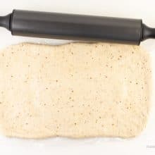 Dough has been rolled out into a long rectangle and sits next to a rolling pin.