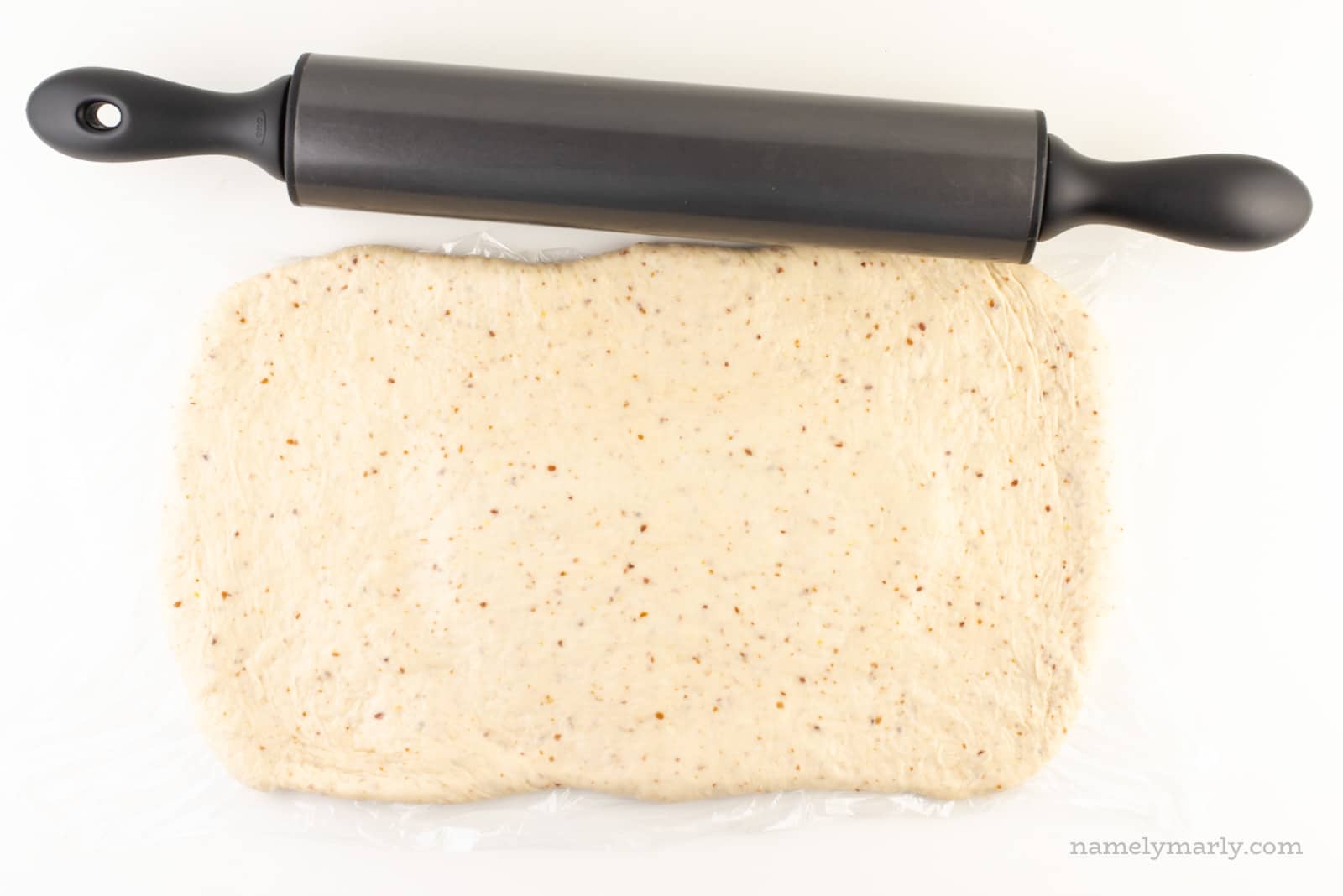 Dough has been rolled out into a long rectangle and sits next to a rolling pin.