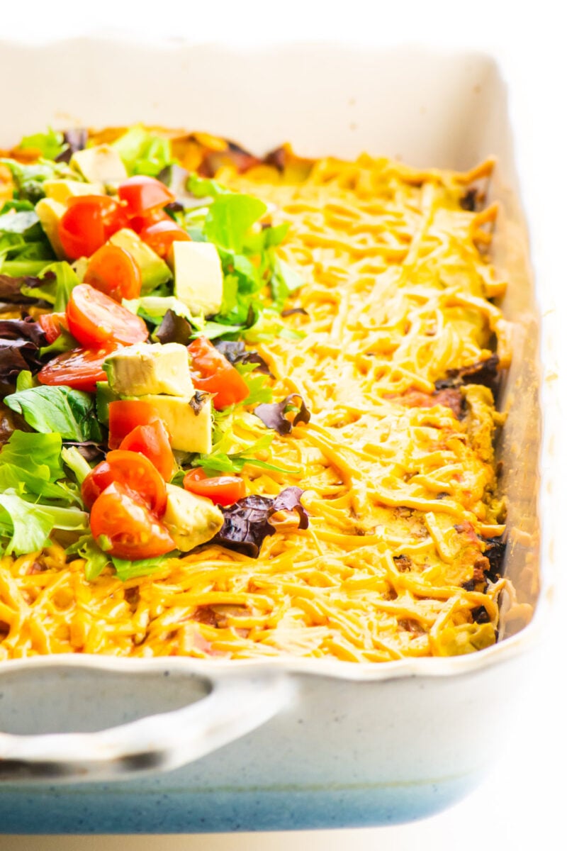 Vegan Mexican Lasagna in a casserole dish with chopped veggies on top.