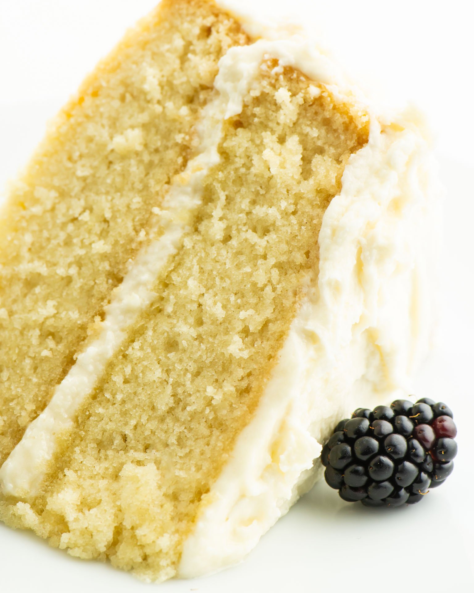 A close-up of a slice of vegan cake with a blackberry sitting next to it.