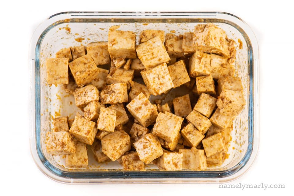 Chopped tofu in a glass container is covered with marinade.
