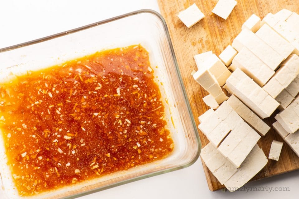 A glass container holds sauce with a cutting board and more ingredients next to it.