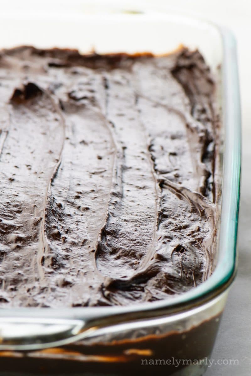 A 9x13 glass cake pan is full of chocolate frosted cake.