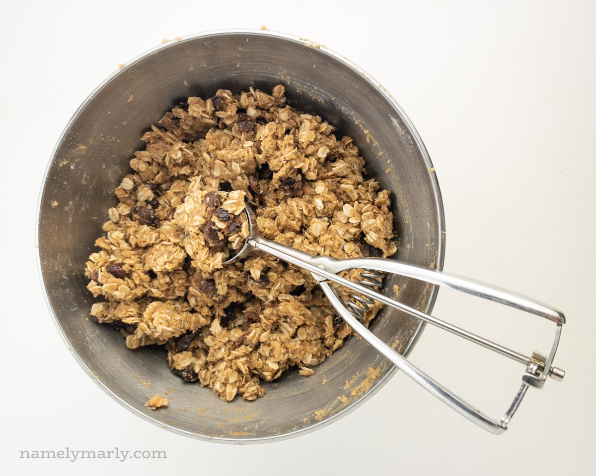 A mixing bowl holds oatmeal cookie dough with a cookie dough scoop in it.