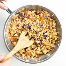 Tofu filling with veggies is in a skillet and a hand holds a spatula stirring it.