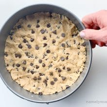 A hand holds a pan full of cookie cake batter with chocolate chips pressed into the top.