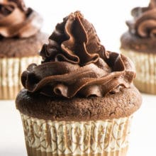 A cupcake with chocolate frosting sits in front of two other cupcakes.