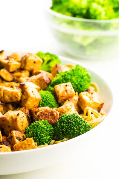 A bowl of cooked tofu with steamed broccoli.
