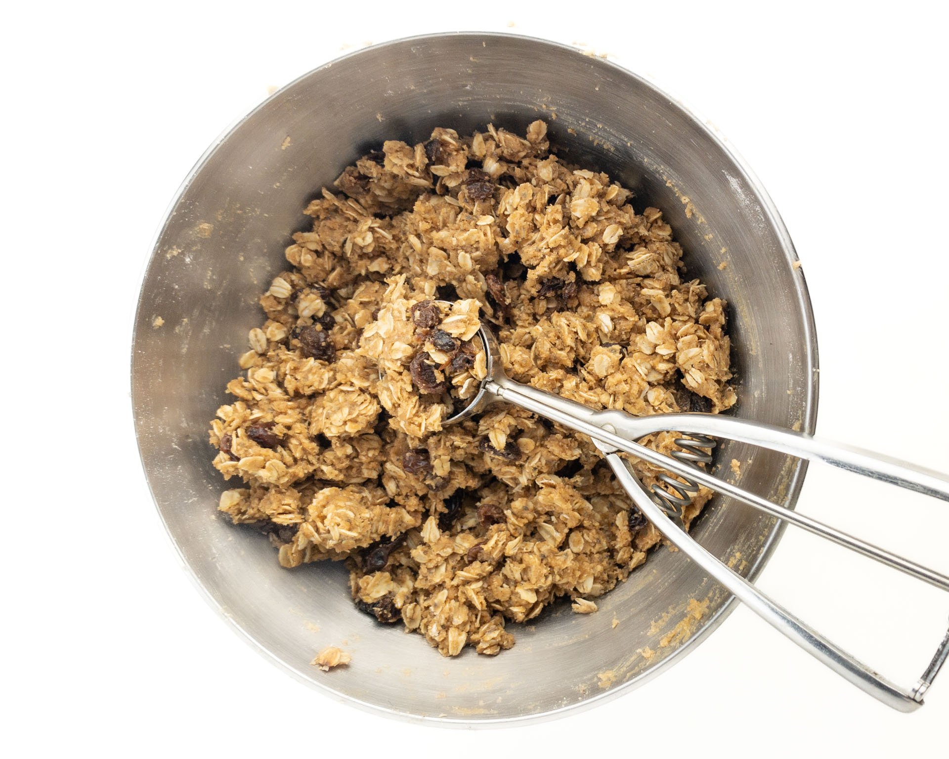 A mixing bowl holds oatmeal cookie dough with a cookie dough scoop in it.