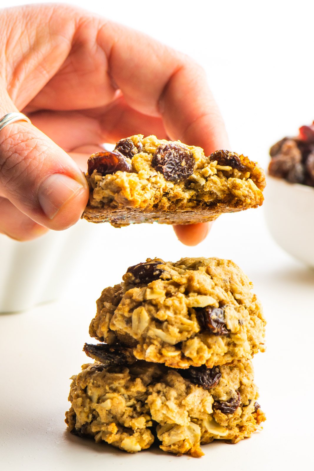 A hand holds a cookie with a bite taken out, hovering over a stack of two more cookies.