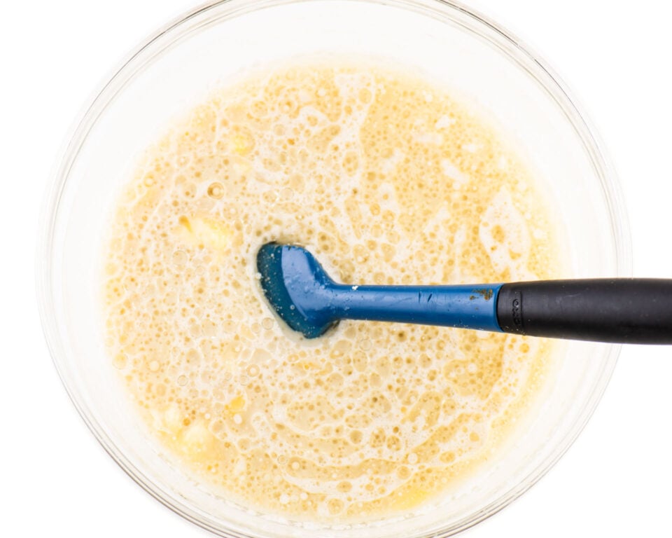 Wet ingredients are combined in a bowl with a blue spatula.