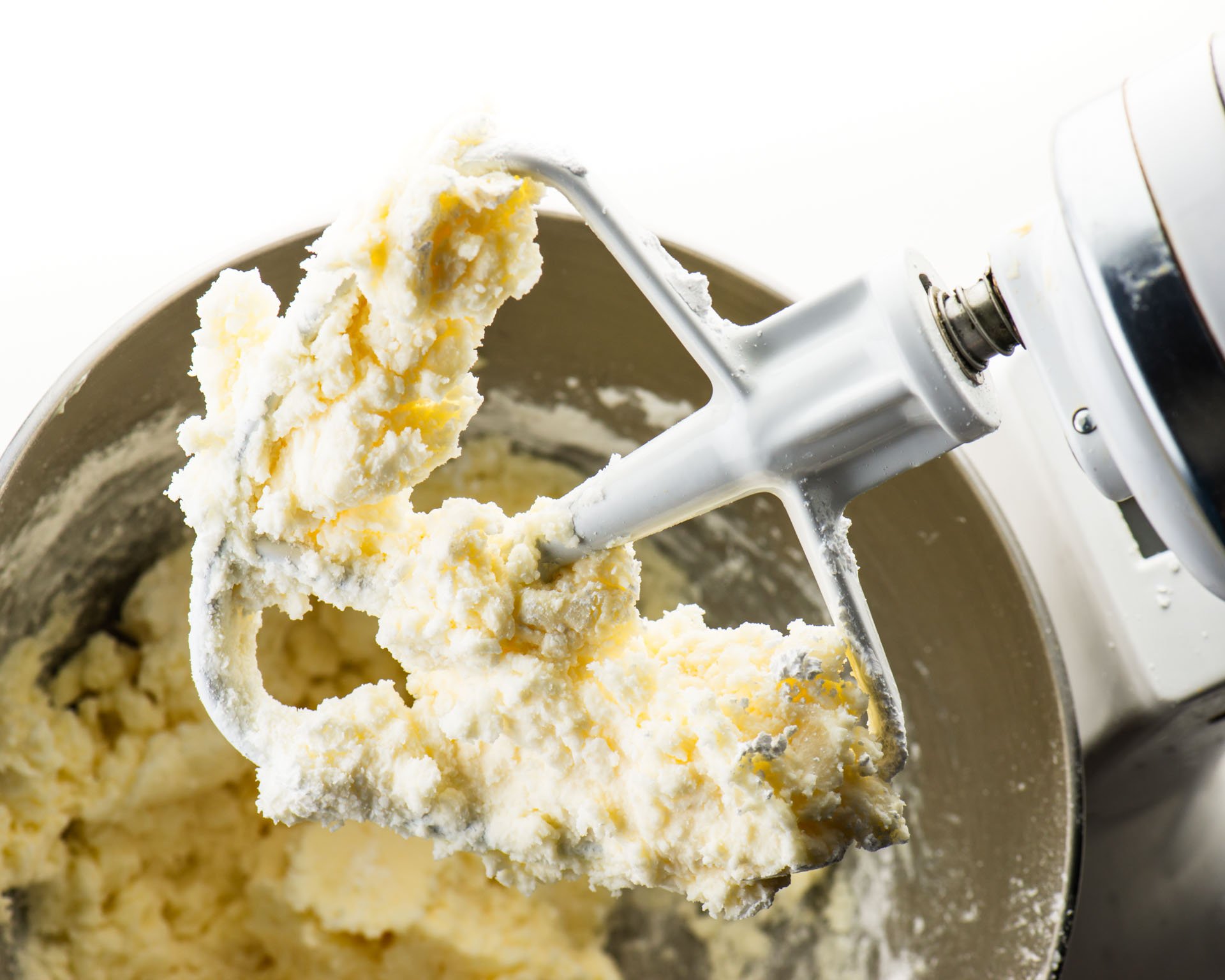 Looking down on a stand mixer with vanilla frosting on the beater.