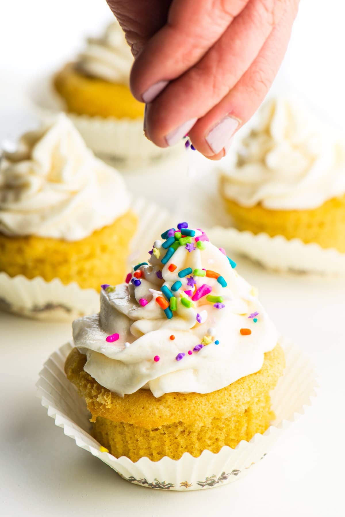 A hand hovers over a cupcake dropping sprinkles on it.