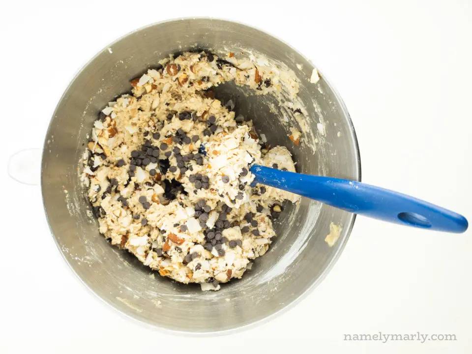 Cookie dough in a metal mixing bowl with a blue spatula.