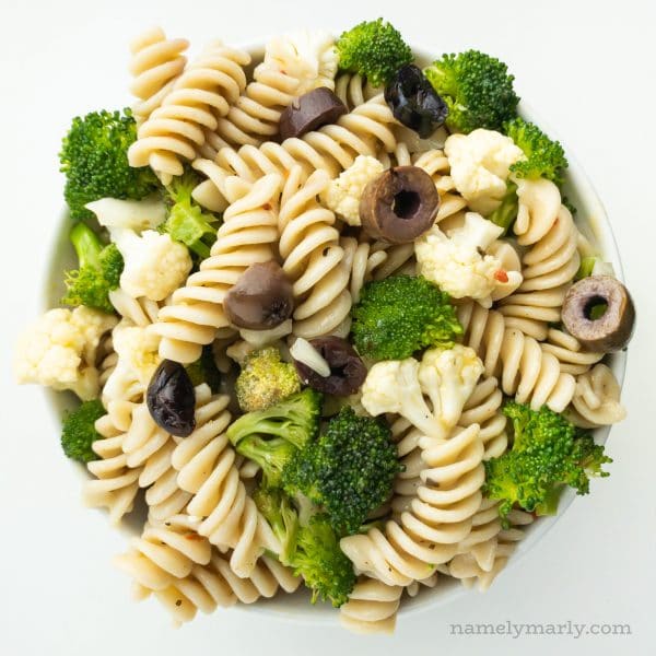 Looking down on a bowl full of pasta salad, showing rotini noodles, broccoli, cauliflower, and black olives.