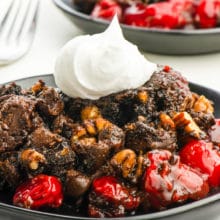 Two servings of chocolate cherry dump cake with whipped cream on top on a table.