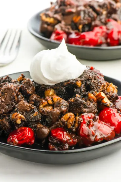 Two servings of chocolate cherry dump cake with whipped cream on top on a table.