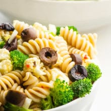 A bowl of pasta salad featuring black olives and broccoli sits in front of another bowl.