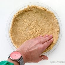 A hand presses the crust into a pie pan.