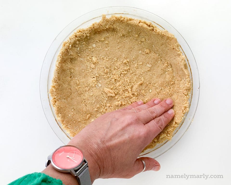 A hand presses the crust into a pie pan.