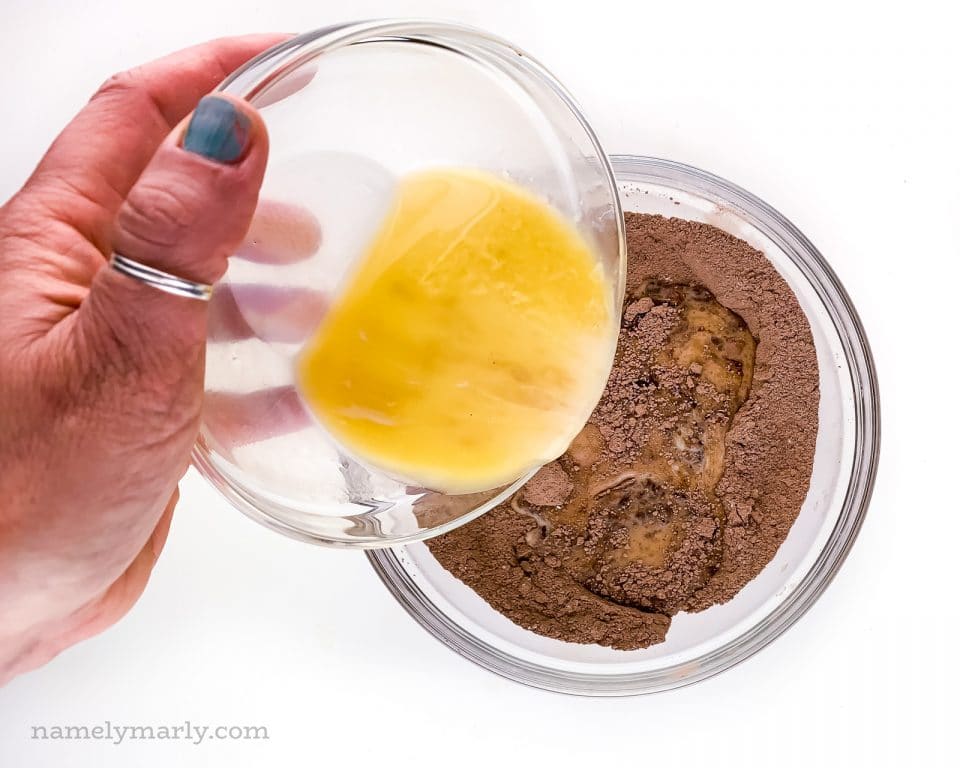 A hand pours melted butter over a cocoa powder base.