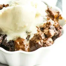 A closeup shot of chocolate pudding cake in a bowl topped with melty vanilla ice cream.